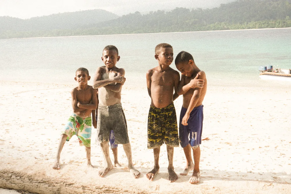 Four boys standing on a white beach.