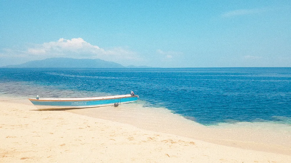 A small boat on a white sand beach beside turquoise water.