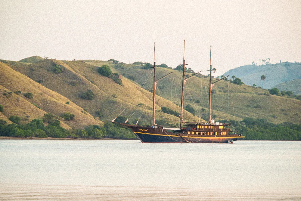 A three-masted phinisi anchored below dry golden hills.