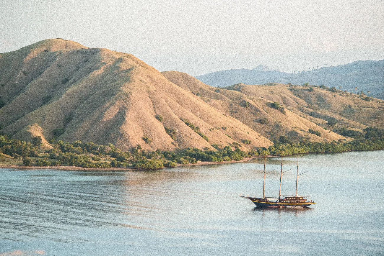 A phinisi at anchor below dry golden hills.